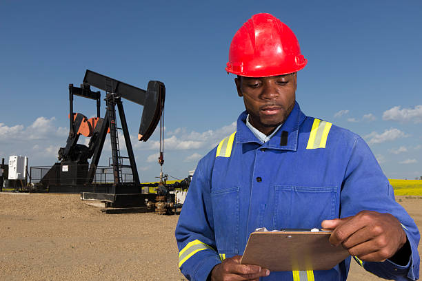 An image from the oil industry of an oil worker in front of a pumpjack holding a clipboard.