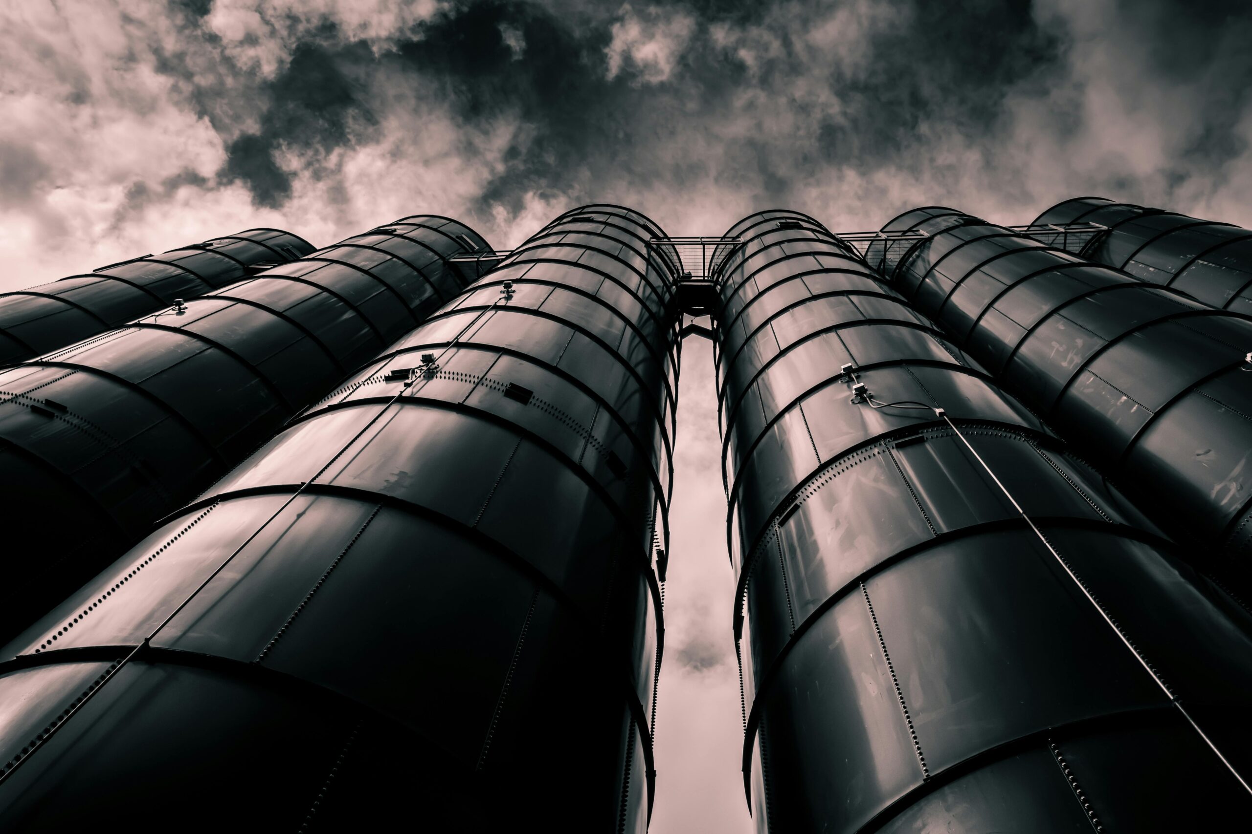 Low angle view of industrial silos with a dramatic cloudy sky in the background, emphasizing modern industry.